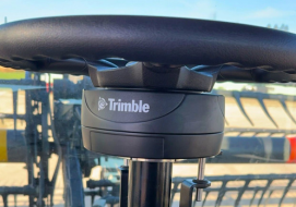 Close-up of a Trimble-branded steering control system installed on a combine, with a clear view of the steering column and part of the vehicle's exterior visible through the windshield.