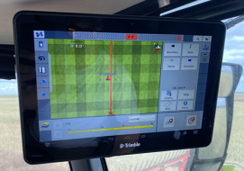 A Trimble touchscreen display mounted inside a claas lexion combine cab, showing a precision agriculture interface with field mapping, navigation lines, and various control options for optimal field coverage.