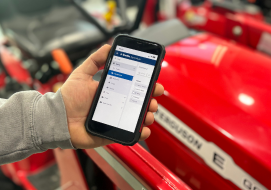 A person holding a smartphone displaying a Trimble interface, with a red Massey Ferguson tractor visible in the background, highlighting mobile precision agriculture control and monitoring capabilities.